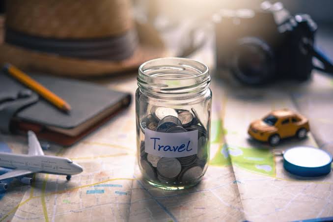 ilustrasi uang dalam tabungan yang dikelililingi transportasi untuk travelling